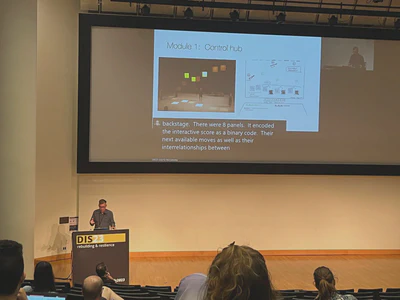 Man giving a presentation in a large white auditorium, with a slide projected on a large screen behind him.